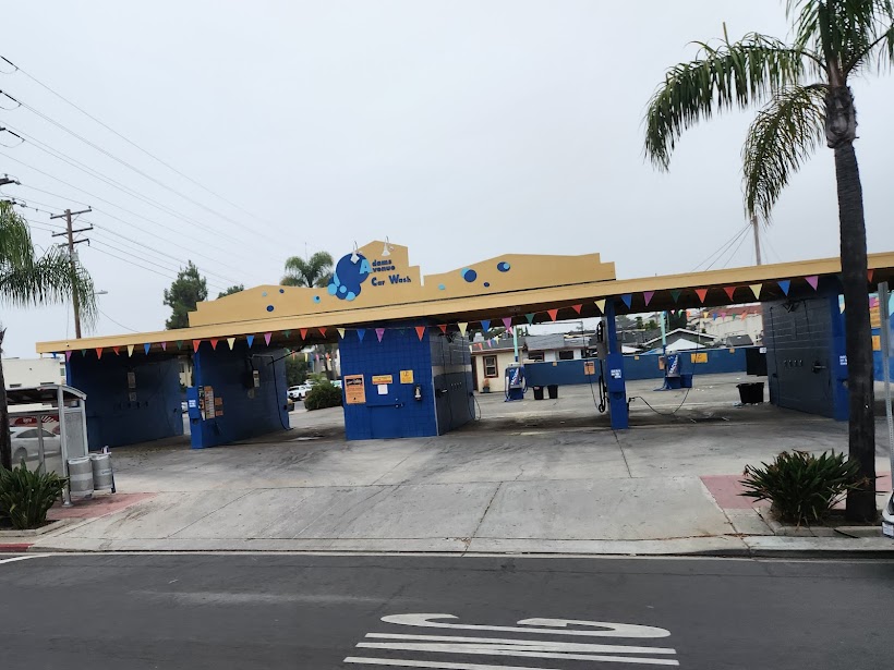 Adams Avenue Car Wash in San Diego – self-service car wash with blue and yellow design, multiple bays, and palm trees in the background.