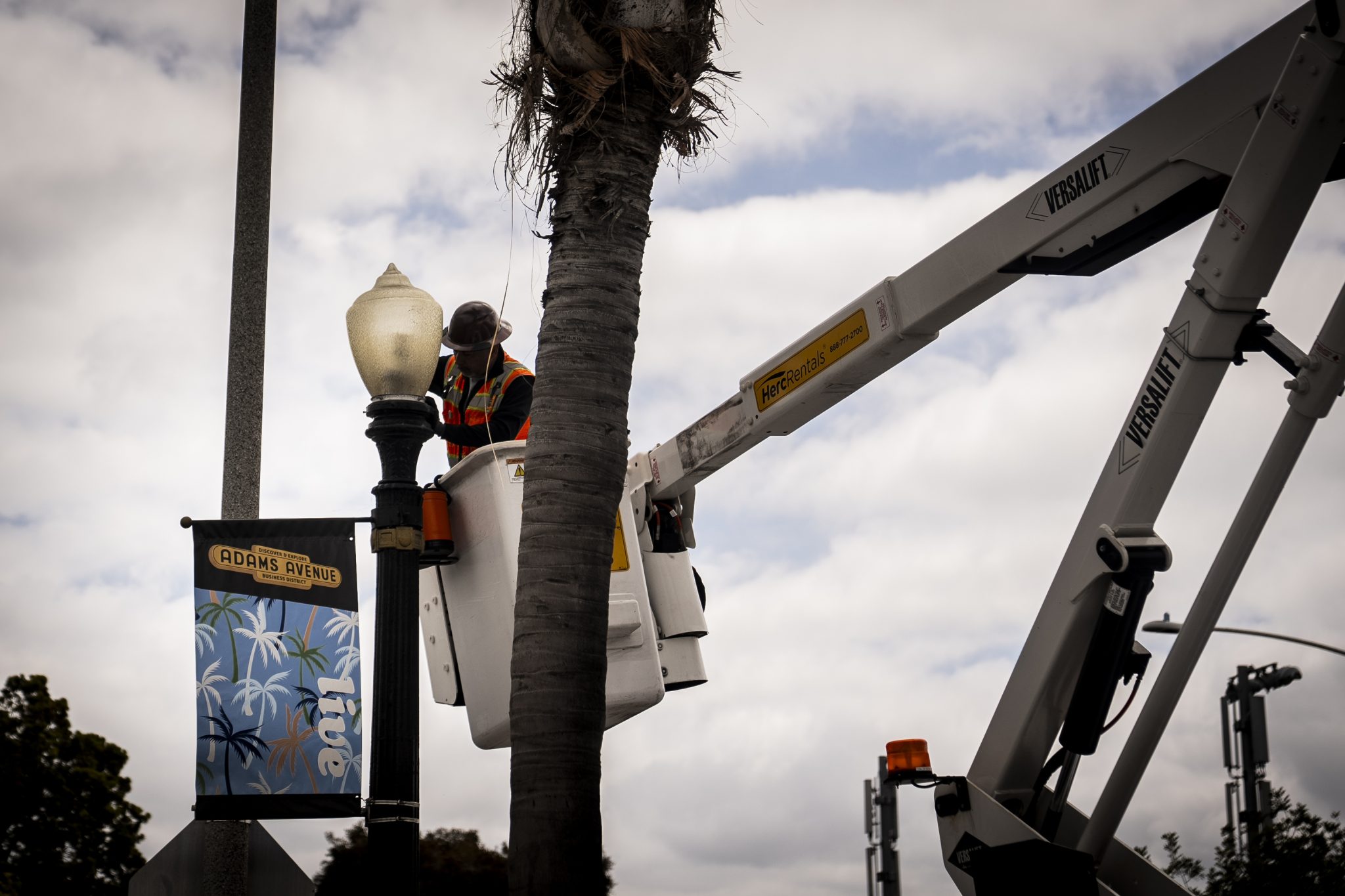 A man fixes a street light next to an Adams Avenue banner