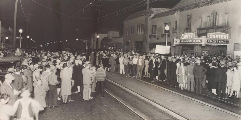 A historic image of crowds waiting along a trolley line outside the Carteri Theater