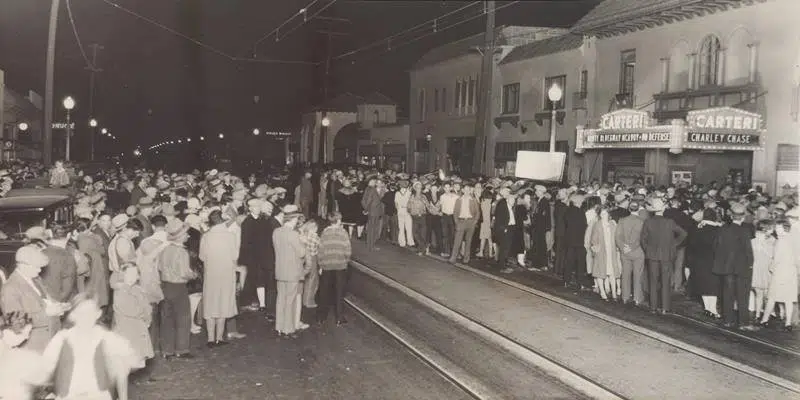 A historic image of crowds waiting along a trolley line outside the Carteri Theater